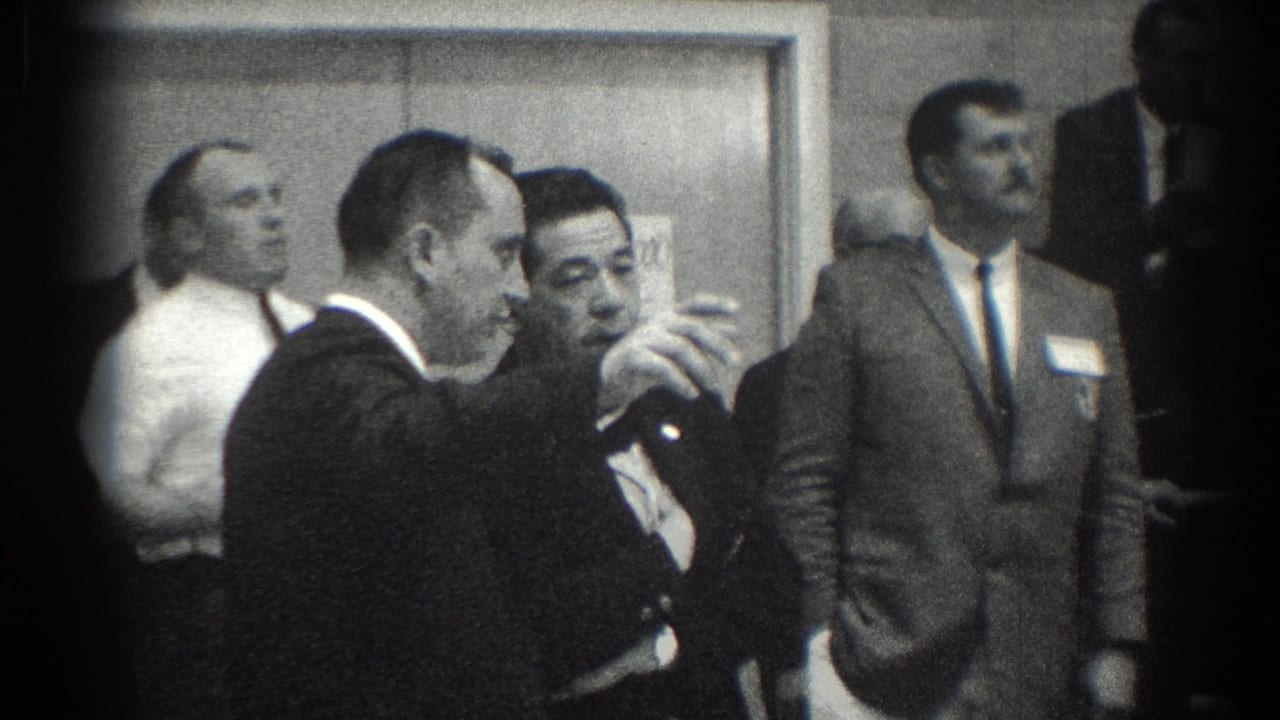 In San Gabriel, California, 1966, suited men converse in a hallway while other attendees stand nearby.