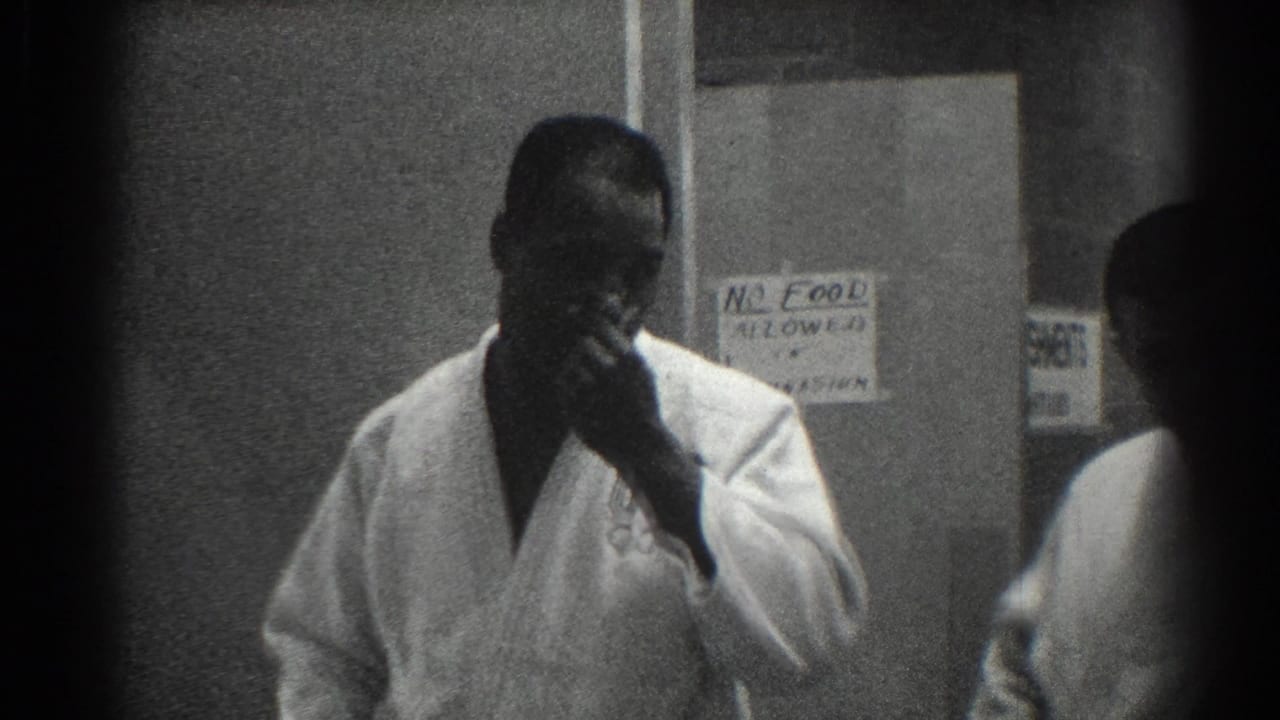 Man in a white martial arts uniform smokes near a posted notice.