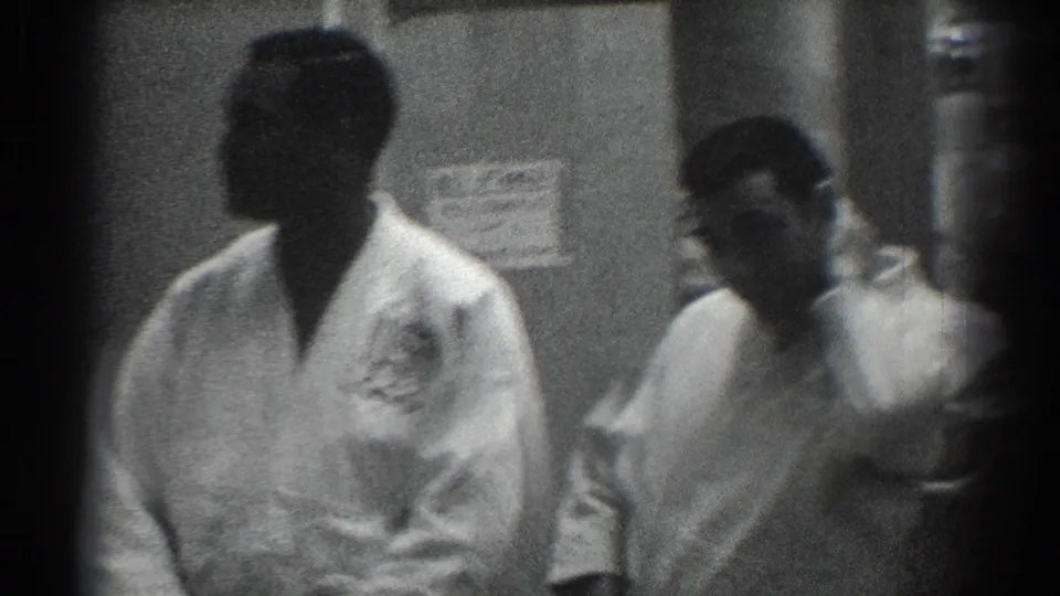 Two men in white martial arts uniforms stand near the camera in grainy 1966 San Gabriel backstage footage.