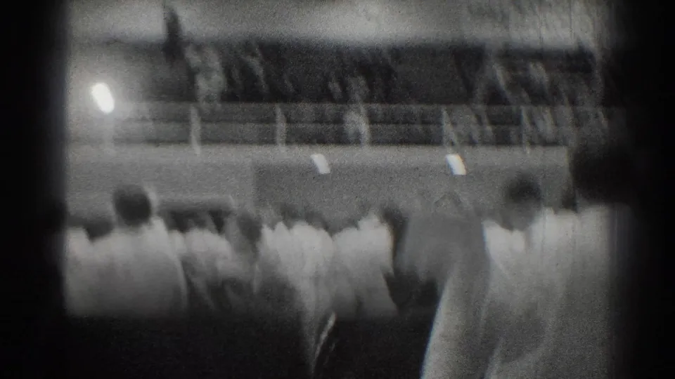 Soft, handheld 8mm view of judo competitors and onlookers inside the San Gabriel gym near the end of the clip.
