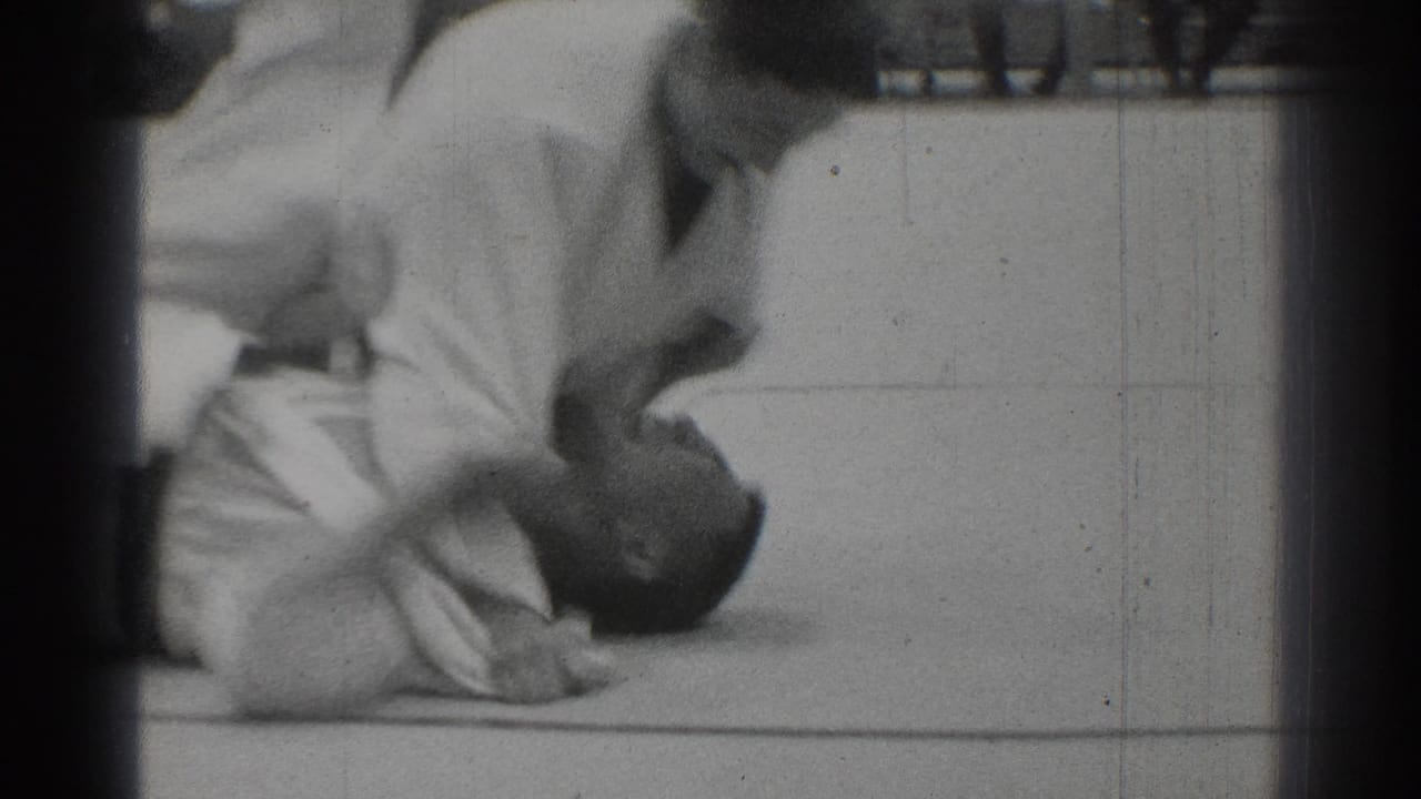 Karate participants on a mat, with one figure low to the floor during a match.