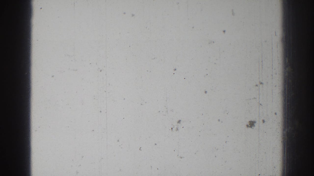 Blank film frame with a broad dark vertical band and small dust marks across the pale surface.