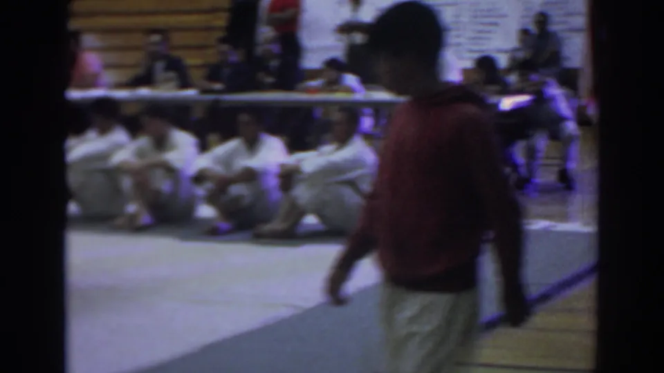 A bystander or participant passes close to the camera during the 1966 Temple City martial arts competition, partly obscuring the seated lineup.