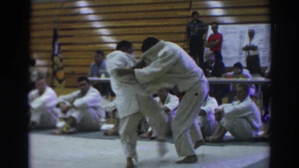A martial artist in a white gi attempts to off-balance an opponent during the Temple City match, with seated participants and officials in the background.