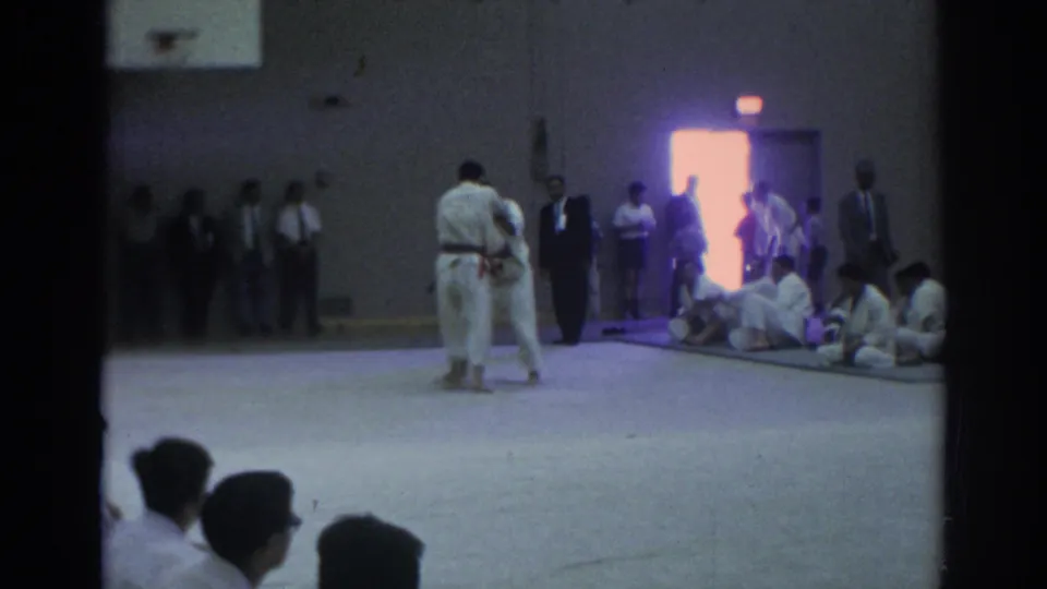 A wide 1966 Temple City gym view shows two judo athletes on the mat, officials standing nearby, and participants seated along the wall.