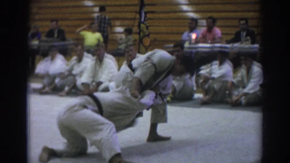 During the 1966 Temple City gymnasium match, one judoka goes down to the mat while the other stands over him after a throw.