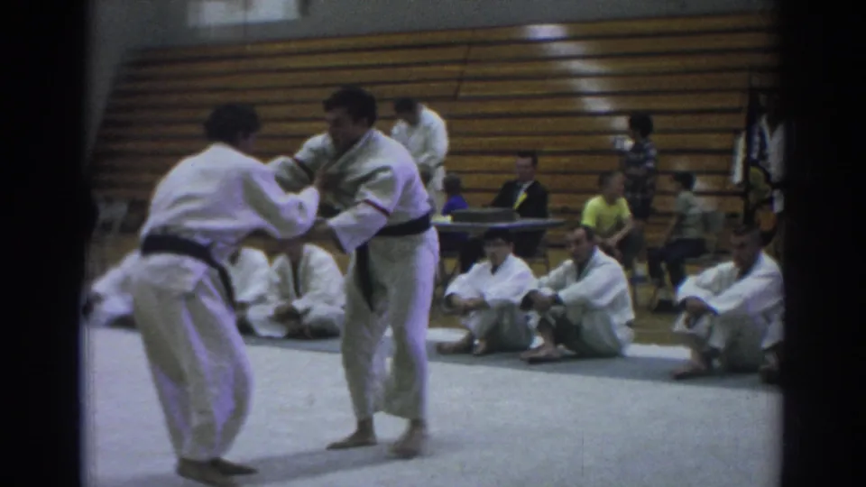 1966 Temple City martial arts demonstration showing two practitioners gripping sleeves or lapels while spectators watch from the mat and bleachers.