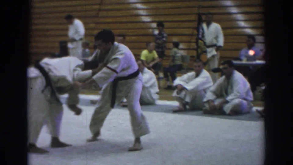 Temple City 1966 8mm frame showing two gi-clad martial artists grappling on a mat as spectators and other participants sit near wooden bleachers.