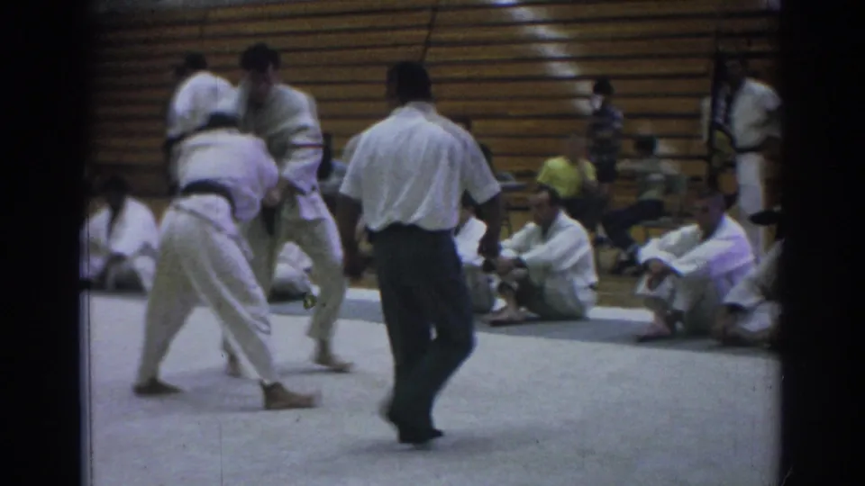 Temple City 1966 8mm frame showing a referee beside two gi-clad competitors as one bends forward during a jujitsu exchange.