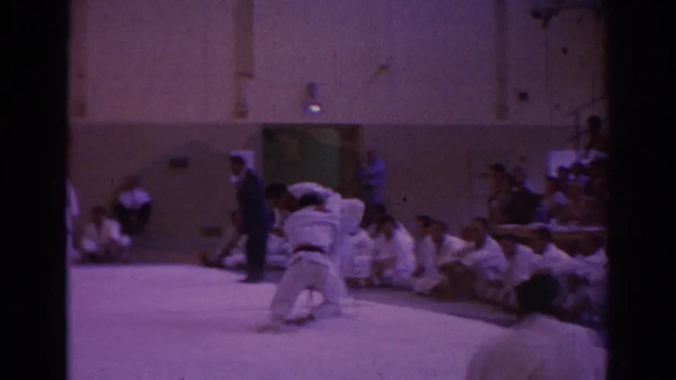 Temple City 1966 indoor martial arts frame showing two competitors on the mat, an official, and spectators along the wall.