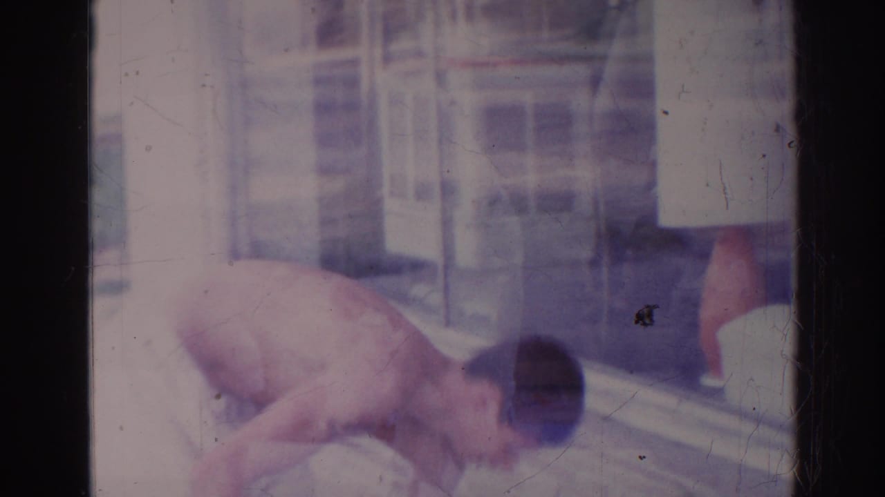 Shirtless man bends beside a storefront window, partly framed by the contact-sheet border.