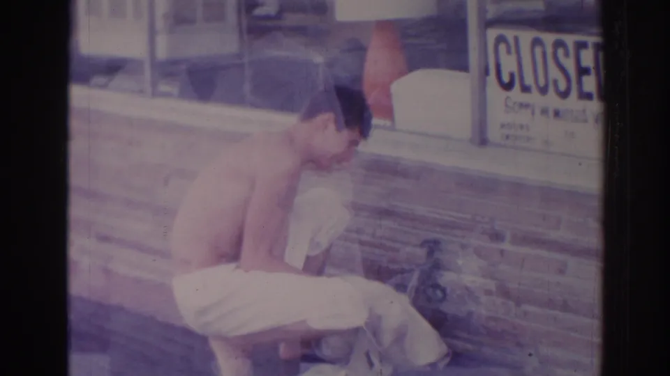 In profile, the man crouches over fabric on the sidewalk outside the Temple City storefront, with the CLOSED sign visible in the window.