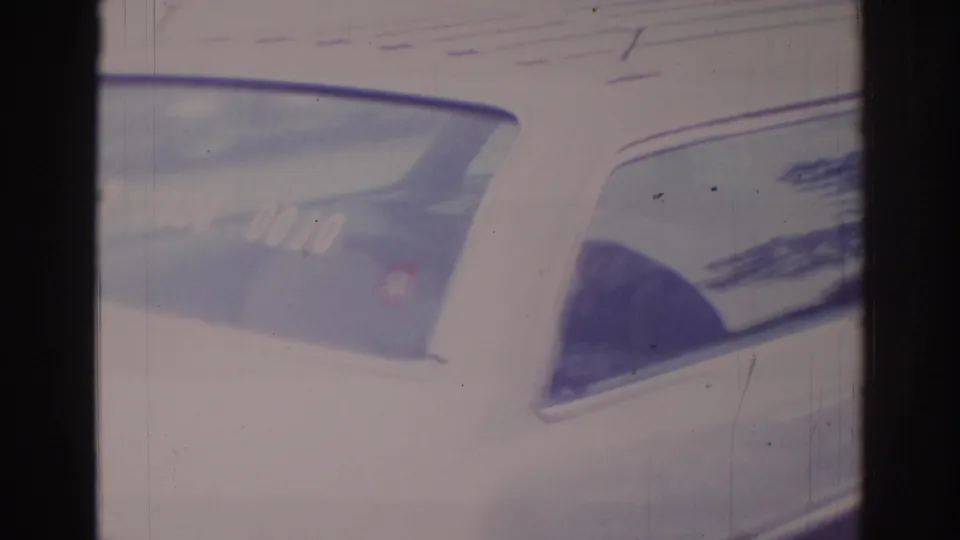 1966 Temple City home-movie frame of a pale sedan, showing the rear side window, roofline, and dojo sticker with visible film grain and scratches.