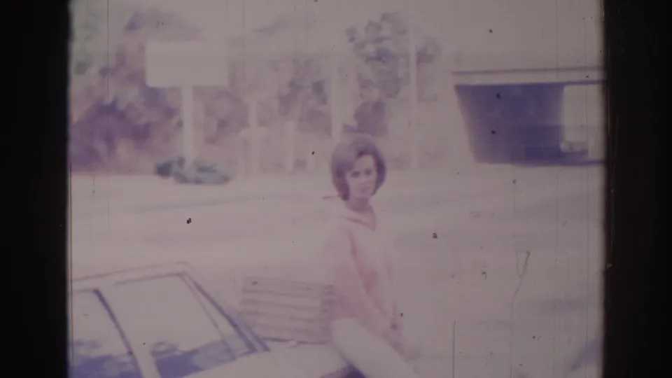 An adult woman in a pink top stands near a car in Temple City, California, holding or carrying a purse.