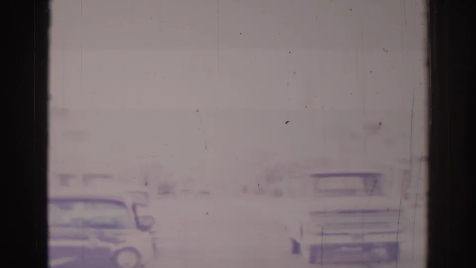 A mid-1960s car appears on a quiet Temple City street, seen through soft, faded 8mm film with roadside signage nearby.