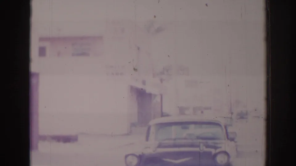 A vintage car sits or moves near the foreground of a 1966 Temple City street scene, with low commercial buildings behind it.