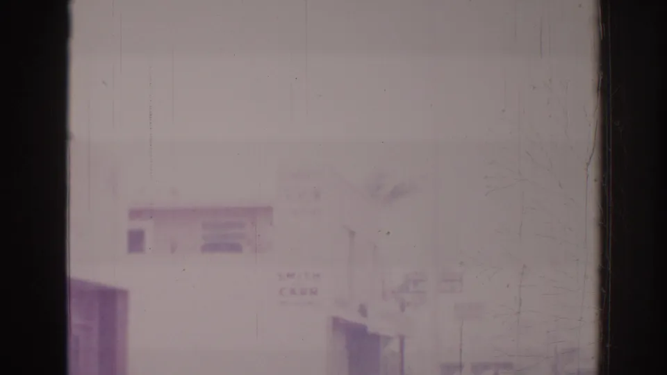 Faded 8mm frame of a quiet Temple City street in 1966, showing low buildings, utility poles, and an indistinct roadside sign.