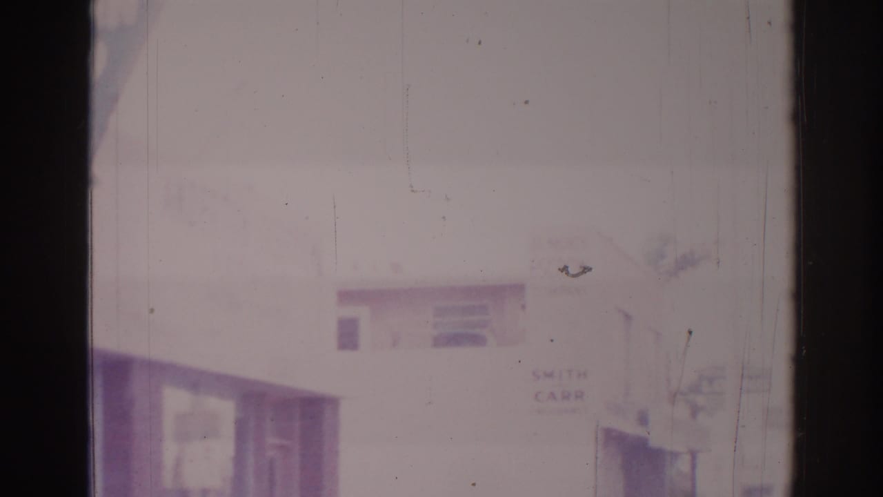Soft 8mm view of a commercial building edge and partial street signage in bright haze.