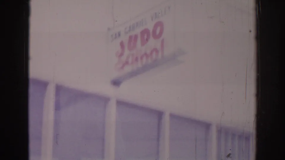 1966 8mm view of the San Gabriel Valley Judo School sign on a Temple City facade with large windows below.