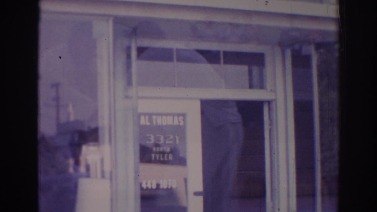 White-framed glass storefront door with painted sign and faint street reflections.