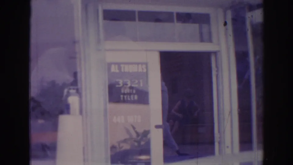 Soft 8mm view of a Temple City glass storefront with posted address text, plant, and reflected men in the panes.
