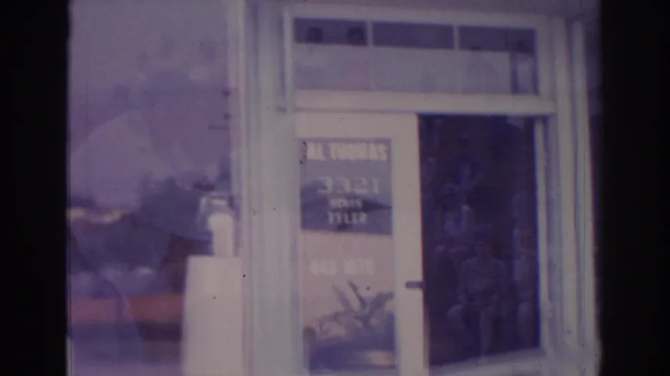 Temple City storefront entrance with painted business lettering, white framing, plant below the sign, and a reflected man at the glass.