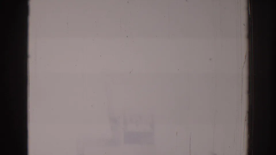 Heavily washed-out 8mm frame from the bus sequence with only faint street forms and visible film wear.