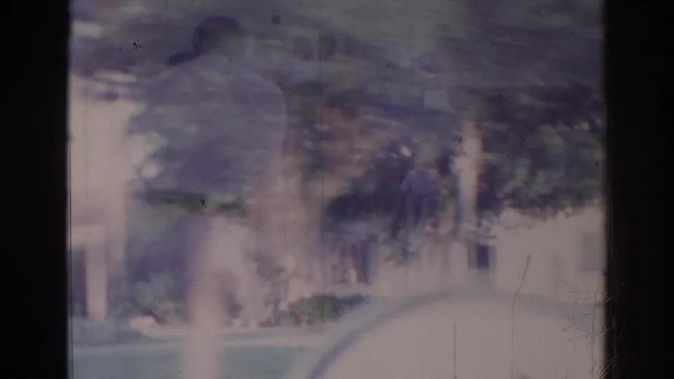 Blurred 8mm frame combines passing trees, lawn, and residential forms in a double-exposed Temple City car-window view.