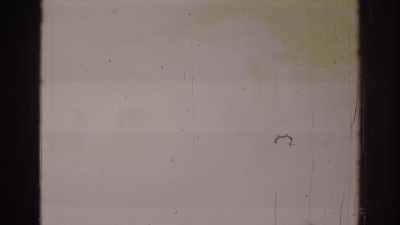 Overexposed pale film frame with dark gate edges, dust specks, and faint horizontal banding.