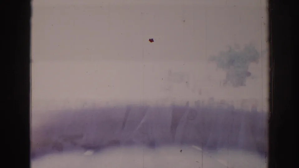 Soft, faded 8mm frame with purple-gray blur, possible light leak, scratches, dust, and dark frame edge.