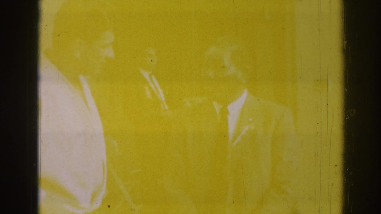 Yellow-tinted, overexposed film frame with faint silhouettes and vertical scratches.