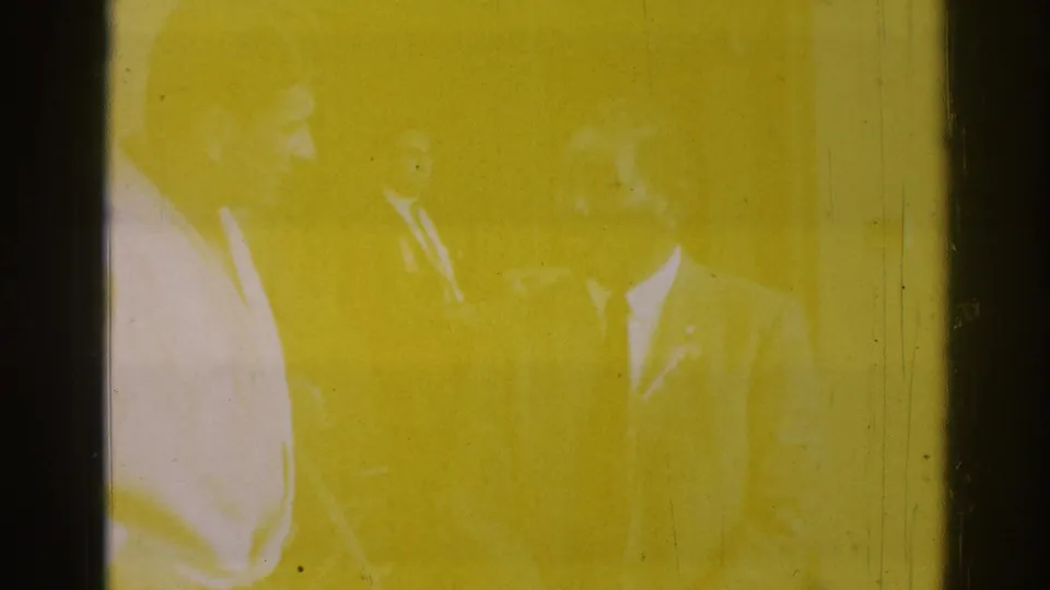A heavily yellow-tinted 8mm frame from the same clip, with faint human forms barely visible through exposure and film staining.