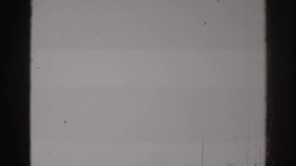 A mostly blank 8mm frame with gray exposure, black film borders, dust specks, scratches, and faint banding from the scan.