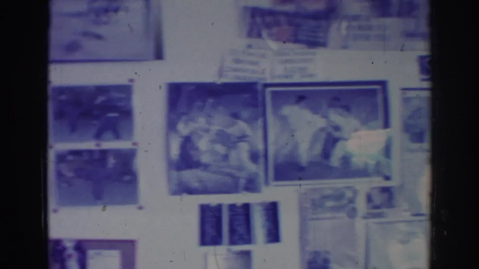 A 1966 home-movie view of a Temple City martial arts school wall showing framed action photos, posters, and printed notices.