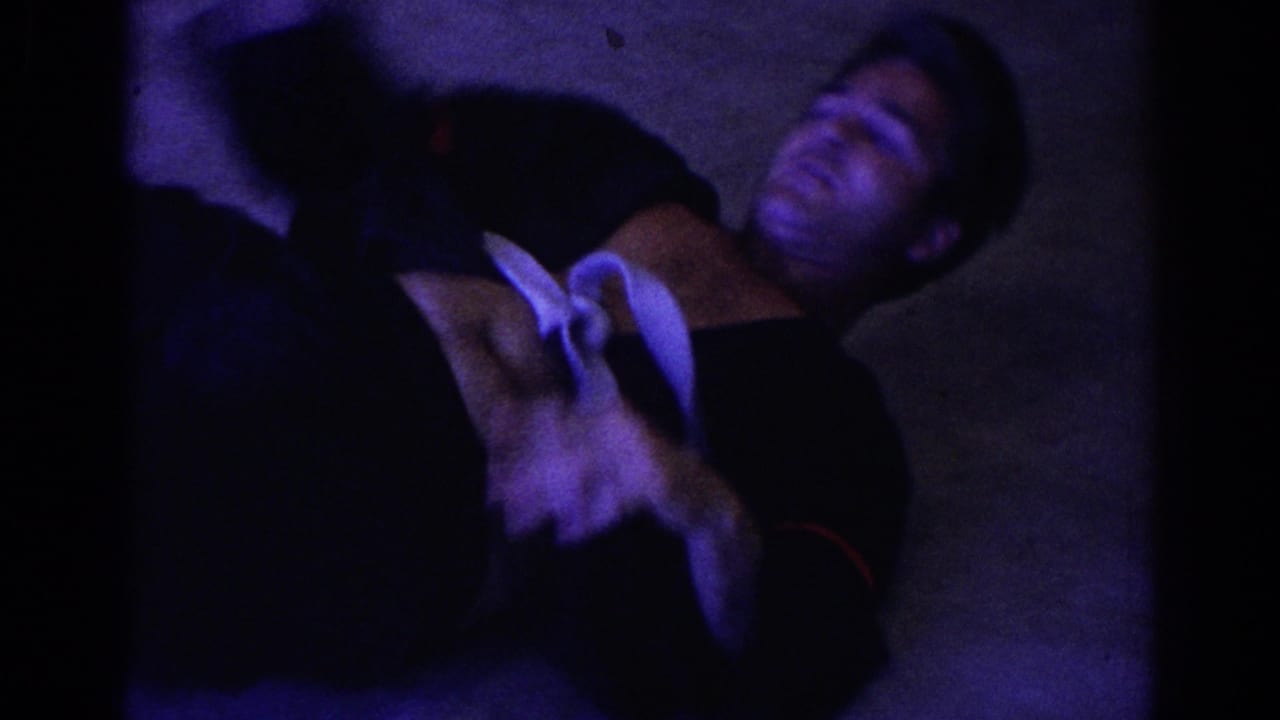 Adult in a dark uniform lies or rolls on the floor during martial arts practice.