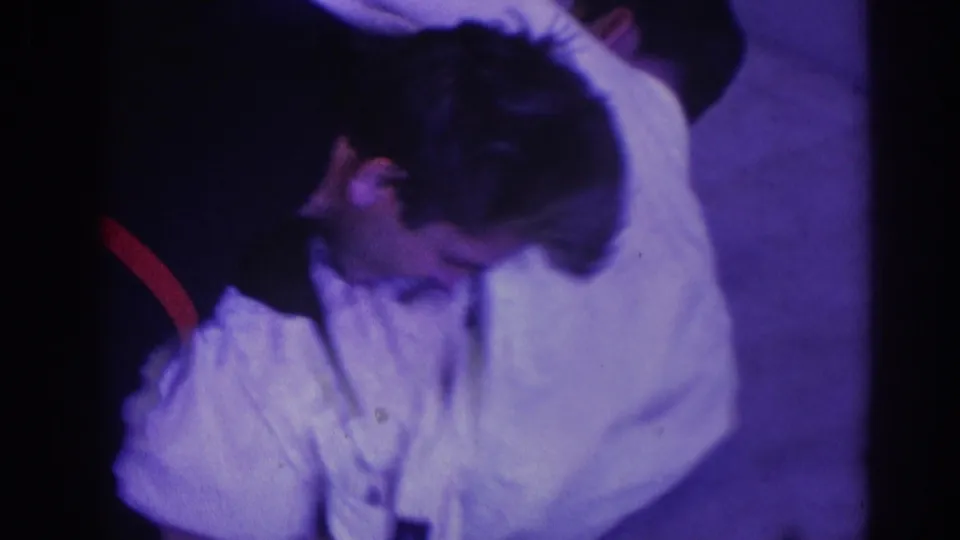 The handheld 8mm frame shows two adult men continuing a floor struggle, with the white gi filling much of the close-up composition.