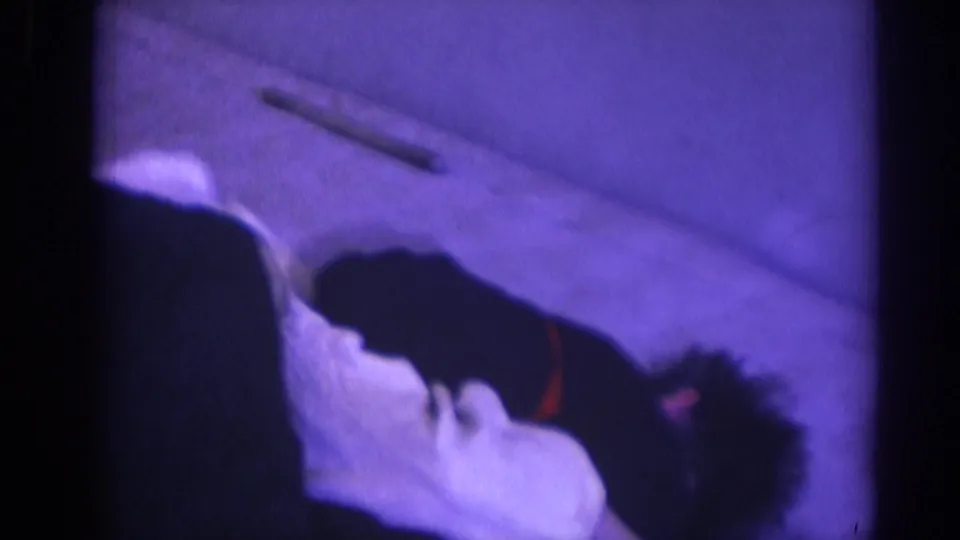 A participant in a white gi lies on the mat while another adult in dark clothing is nearby in the 1966 indoor match footage.