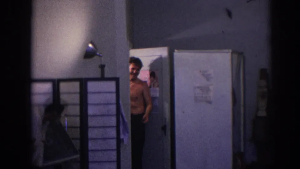 1966 Temple City home-movie frame with a shirtless young man at a doorway beside a folding screen in a private room.