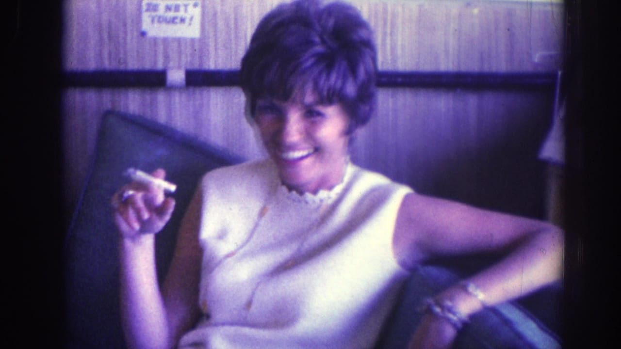 Woman in a white sleeveless dress laughs while holding a cigarette indoors.