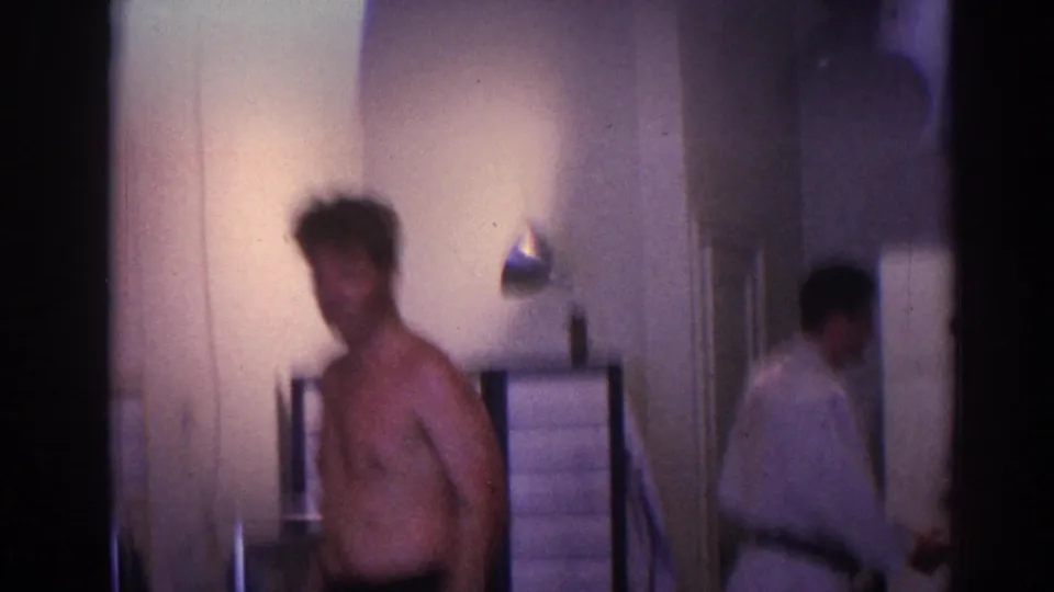A shirtless man stands in a private interior, with another person partly visible near a doorway in the 1966 Temple City footage.
