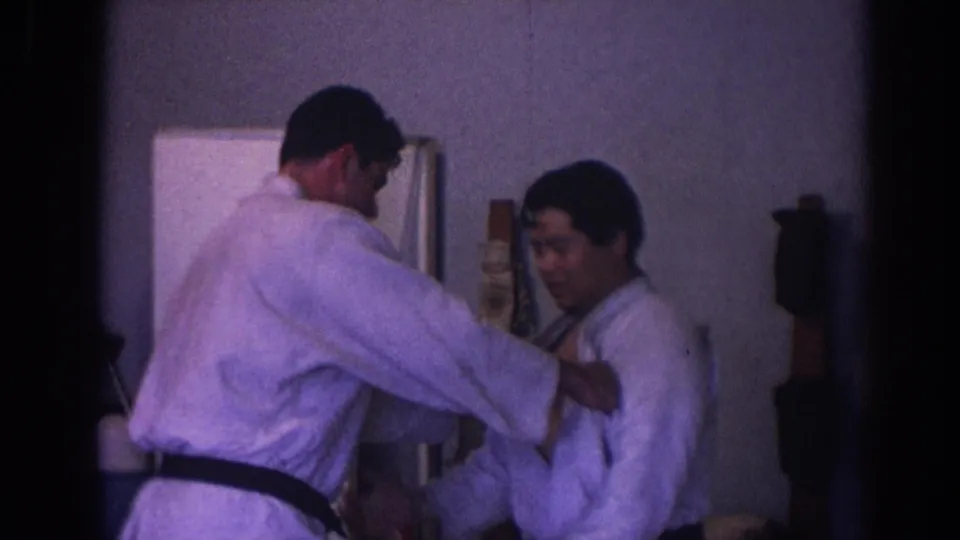 Two men in white judo uniforms practice a technique indoors in the 1966 Temple City home-movie footage.