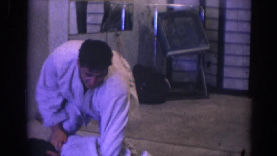 1966 Temple City frame showing a man in a white gi applying or demonstrating a grappling hold on the mat in a small dojo.