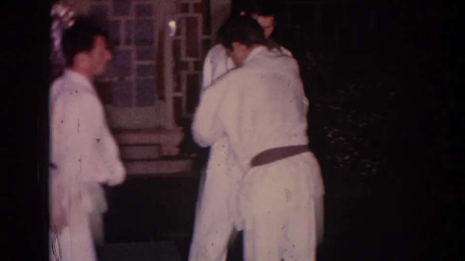 1966 Temple City frame showing people in white gi gathered near a doorway or shoji-style screen after the martial arts demonstration.