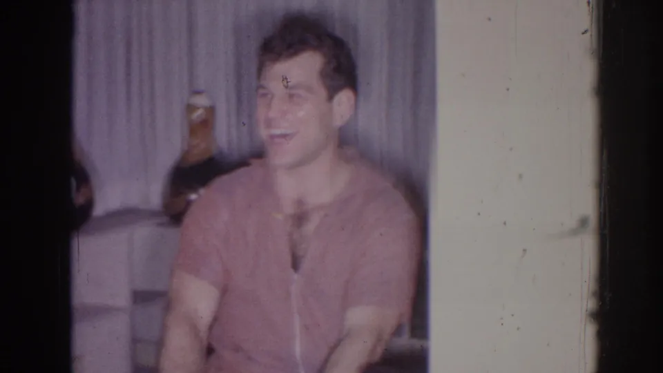 The seated man smiles toward someone off camera while holding the small drum in the Temple City home setting.