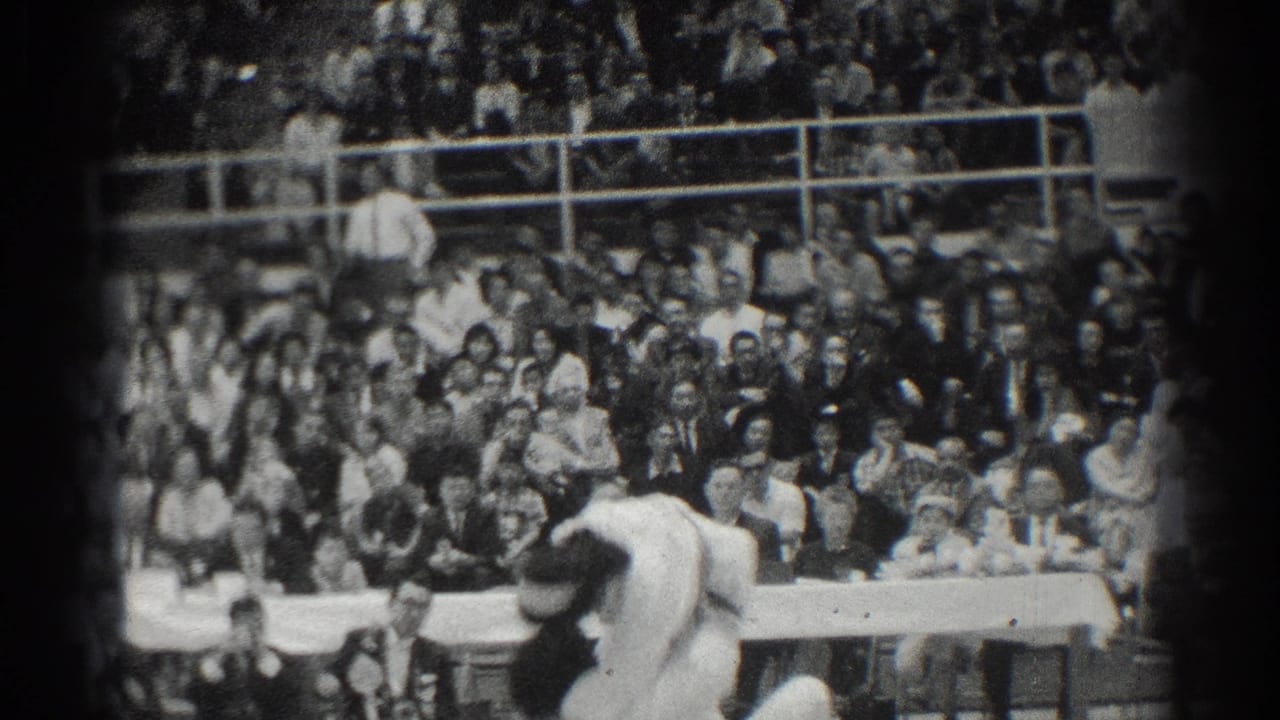Two martial artists grapple near a crowded audience and bleachers.