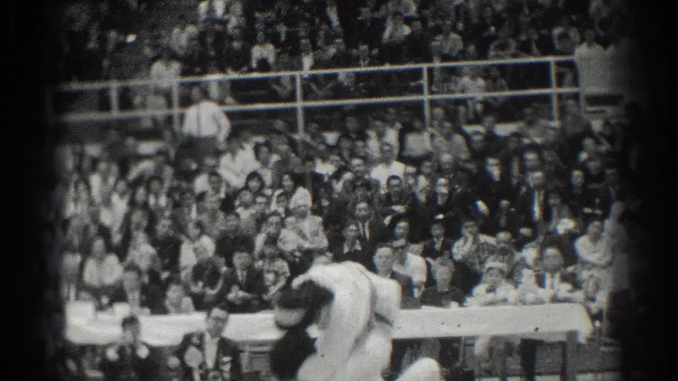 In West Covina, California, two athletes in white uniforms grapple during a 1966 karate match before spectators.