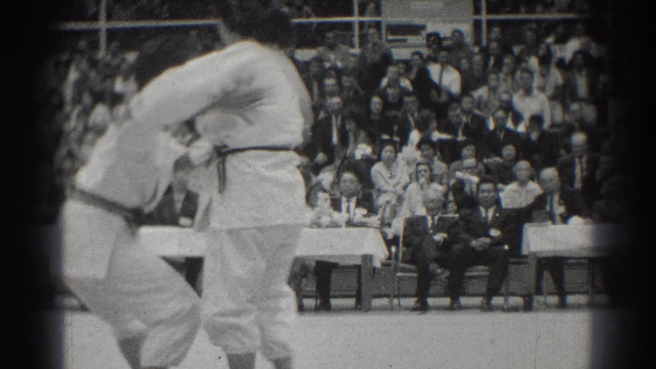 Two uniformed competitors clinch in front of seated spectators and officials.
