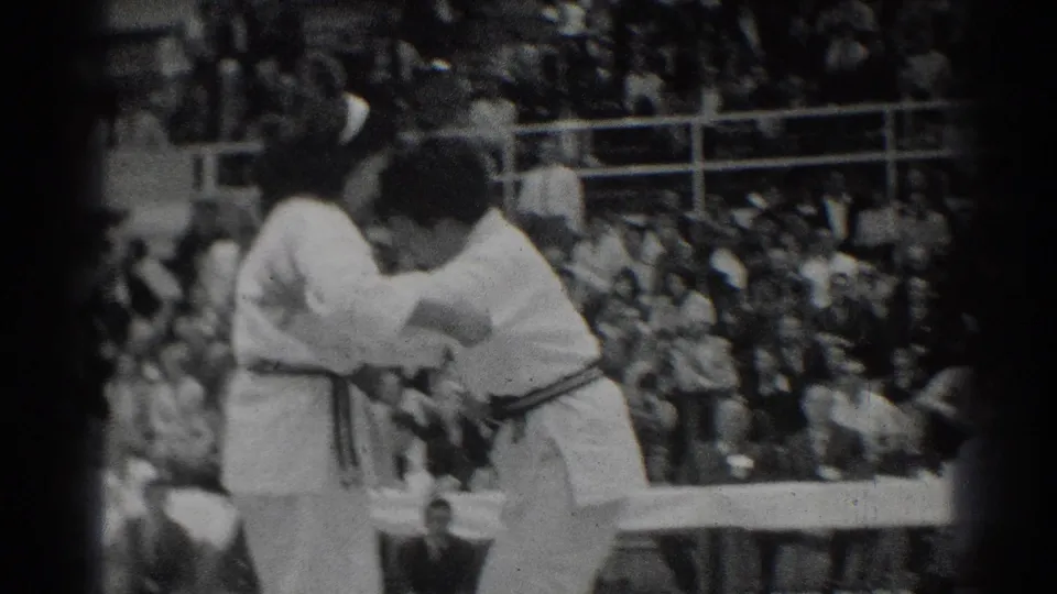 A close spectator-side view shows the competitors upright and locked together during the 1966 karate match.