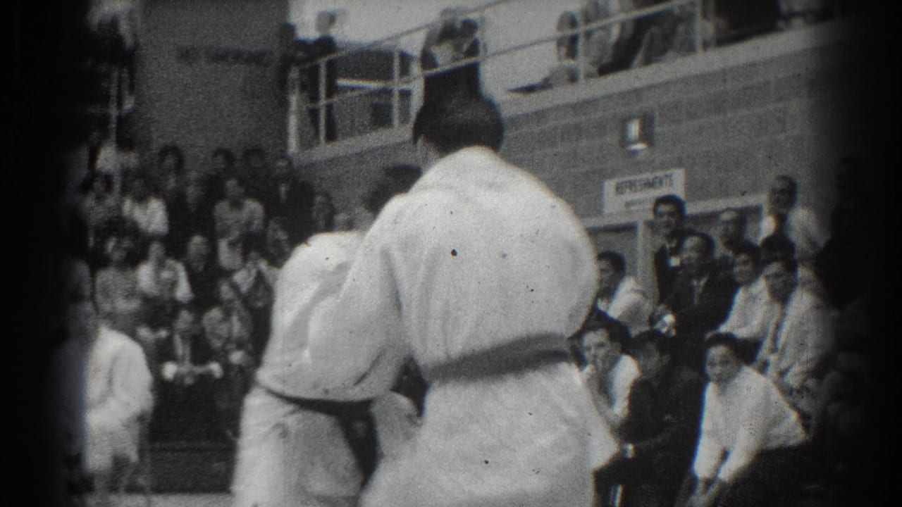 Karate competitors in white uniforms face each other near a seated audience.