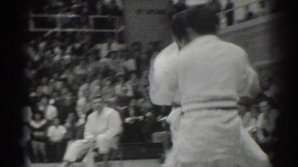 A rear view of a white-gi competitor frames the seated audience during the 1966 West Covina karate competition.